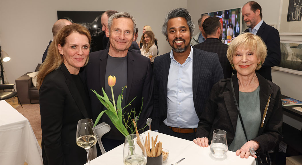 Get together im Wiener Atelier mit BrandTrust Veranstaltungsteilnehmer stehen zusammen mit Colin Fernando am Tisch und lächeln.