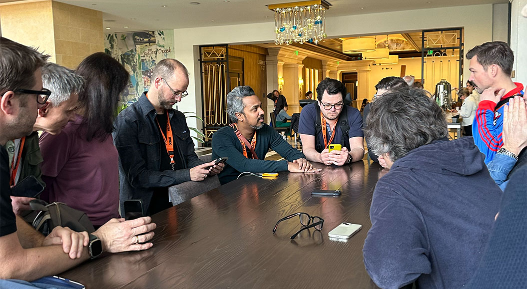 Mehrere Personen sitzen an einem Tisch während eines Vorbriefings. Alle tragen Lanyards mit Ausweismarken.