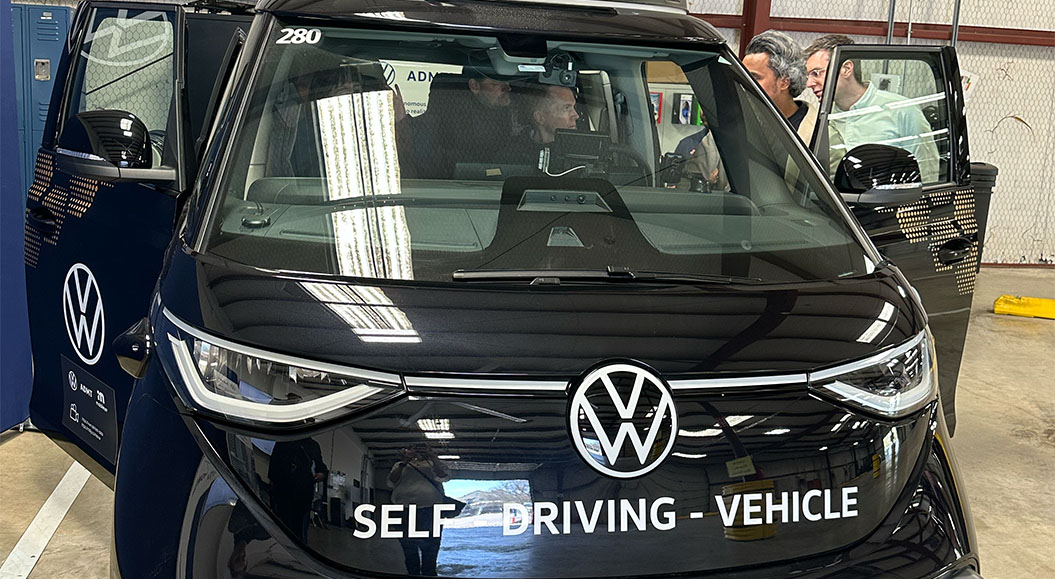 eine Person im Fahrzeug, mit einem klaren Blick auf das Fahrzeuglogo und den Schriftzug „Self-Driving Vehicle“