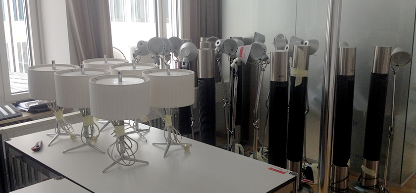 Mehrere Lampen und Turmventilatoren stehen auf einem Tisch in einem Büro. Das Bild zeigt den Umzugsprozess der Nürnberger Filiale von Brand Trust, bei dem die Möbel und Geräte in den neuen Raum transportiert werden.