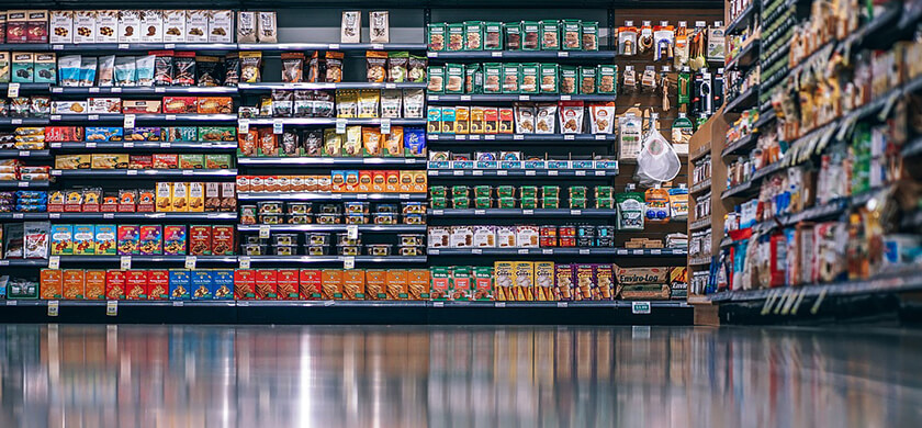 @igorovsyannykov / Pixabay Supermarktregal mit verschiedenen Packungen von Snacks, Süßigkeiten, Keksen und anderen Lebensmitteln. Die Regale sind gut strukturiert, mit farbigen Verpackungen und Preisschildern, die deutlich sichtbar sind. Der Boden ist reflektierend, was eine klare Spiegelung des Regals zeigt.